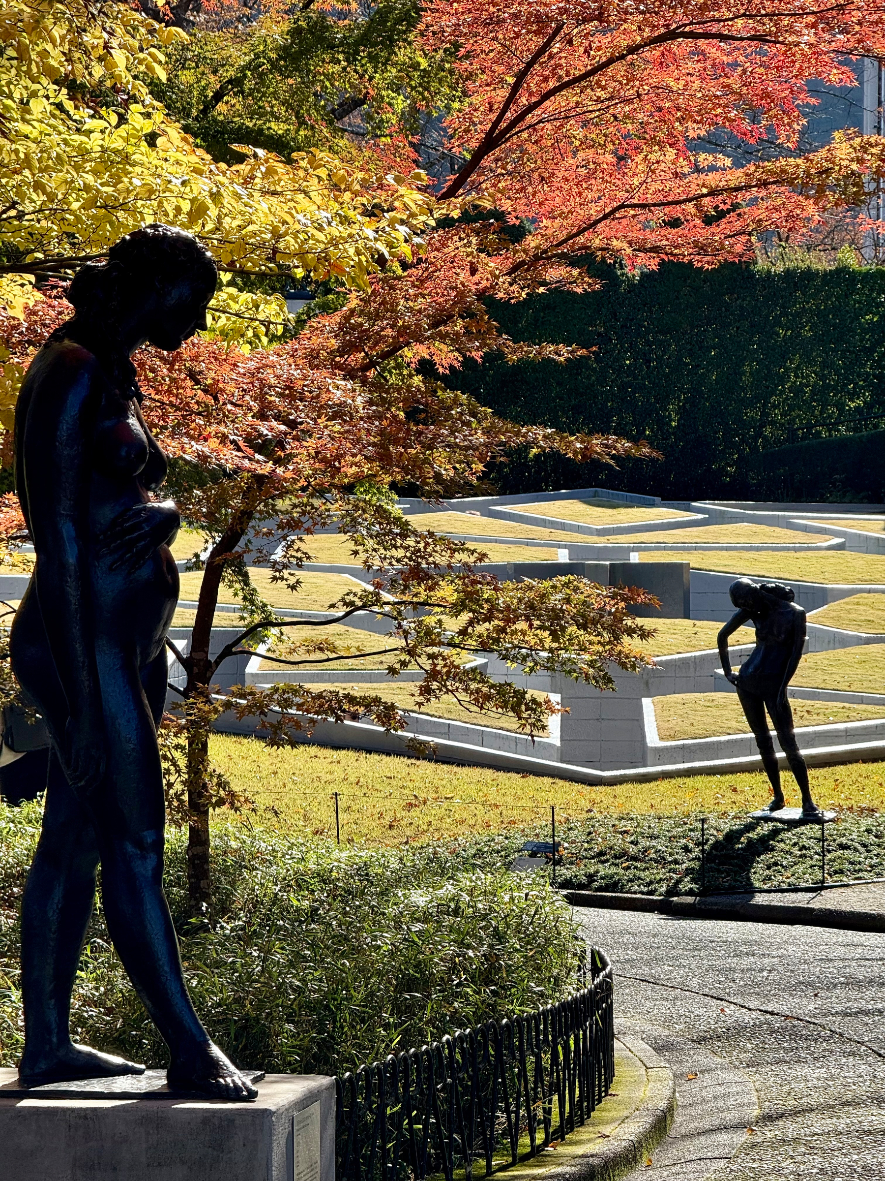 Bronze statues stand in a scenic garden with vibrant autumn foliage and manicured hedges.